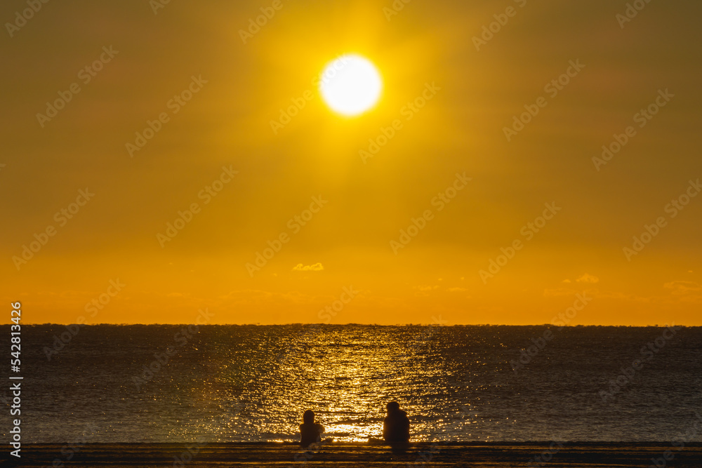 Silhouette of two people sitting on the beach just after sunrise