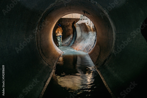 Sewer tunnel worker examines sewer system damage and wastewater leakage