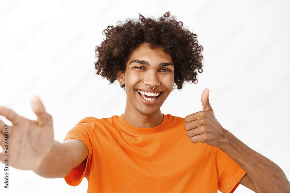 Close up portrait of hispanic guy video chat, holding mobile phone and waving at camera, laughing and smiling, standing over white background Close up portrait of hispanic guy video chat, holding mobile phone and waving at camera, laughing and smiling, standing over white background