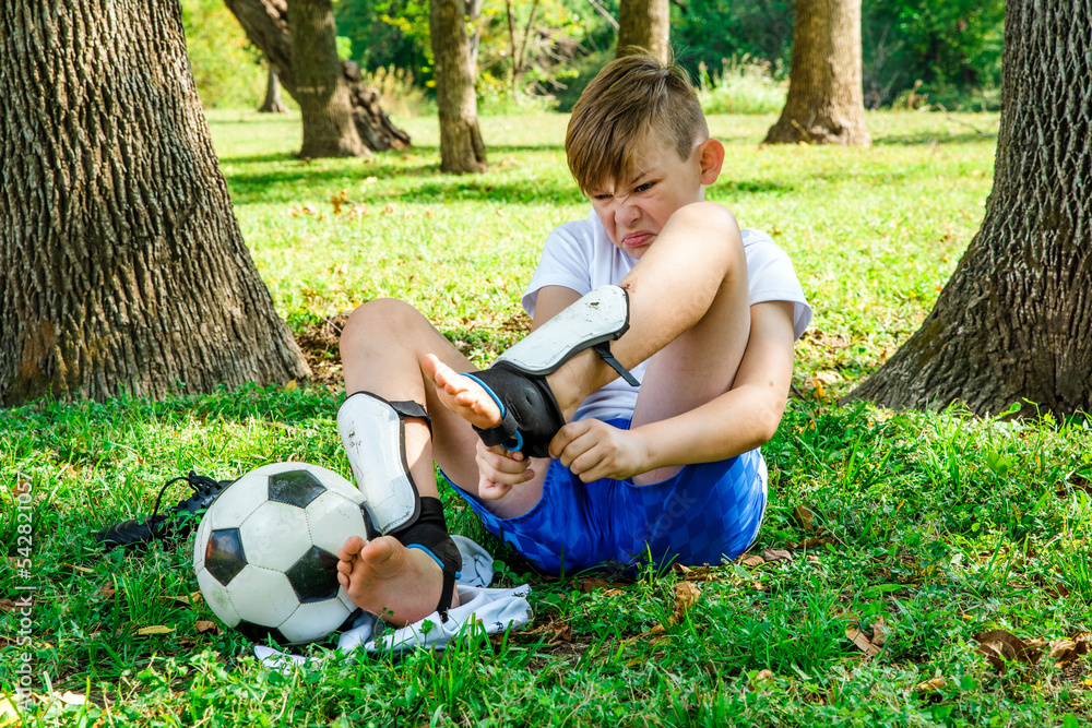 Boy soccer player struggling to put on his shin guards and soccer socks