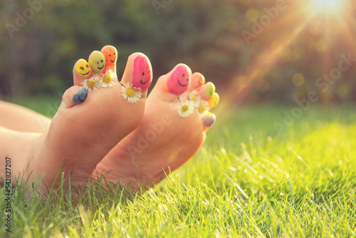 Teenage girl with drawn smiling faces and chamomiles between toes outdoors, closeup. Space for text © New Africa