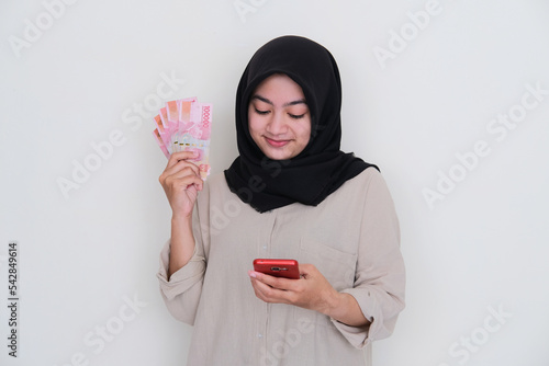 Young moslem girl holding money while using her mobile phone photo