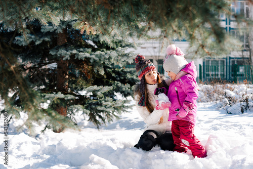Caucasian woman and her little daughter hugging smiling having fun in sunny winter day. Horizontal headshot, side view. Blurred background. Happy parenting and winter activities concept.
