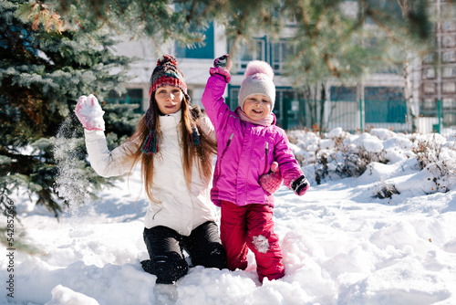 Caucasian woman and her little daughter looking at camera smiling having fun in sunny winter day. Horizontal headshot, side view. Soft focus on kid. Happy parenting and winter activities concept.