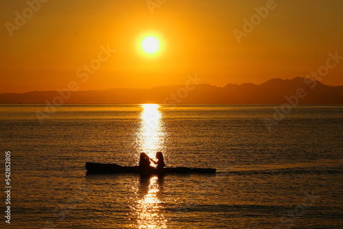 Fototapeta Naklejka Na Ścianę i Meble -  夕暮れの逗子海岸、オレンジ色に染まる海でカヤックを楽しむ若者