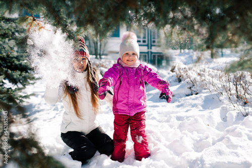 Caucasian woman and her little daughter looking at camera smiling having fun in sunny winter day. Horizontal headshot, side view. Soft focus on kid. Happy parenting and winter activities concept.