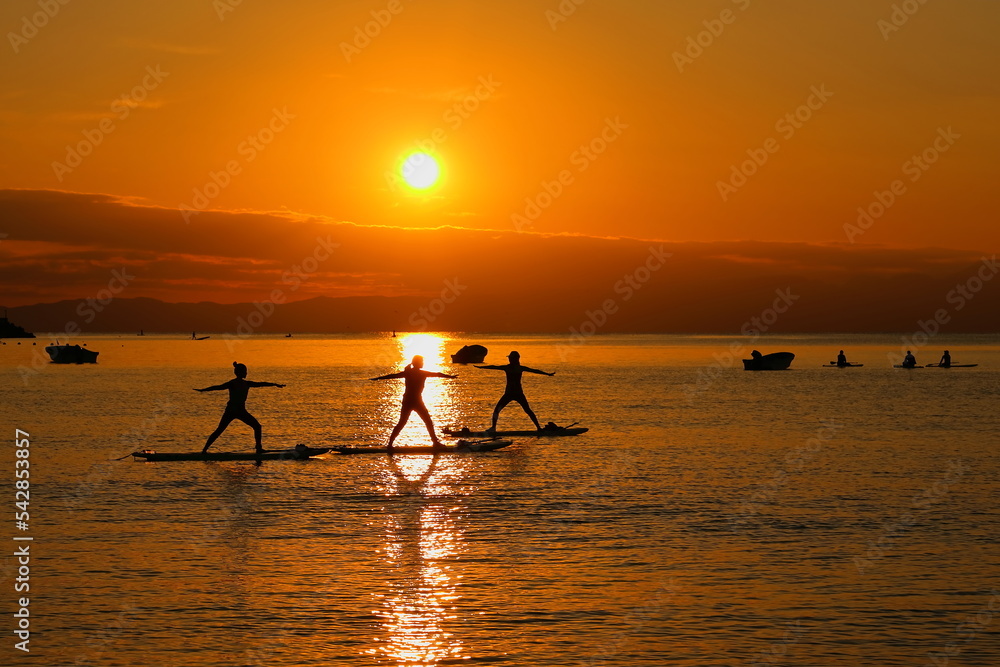 夕暮れの逗子海岸、オレンジに染まる海でSUPヨガを楽しむ女性たち
