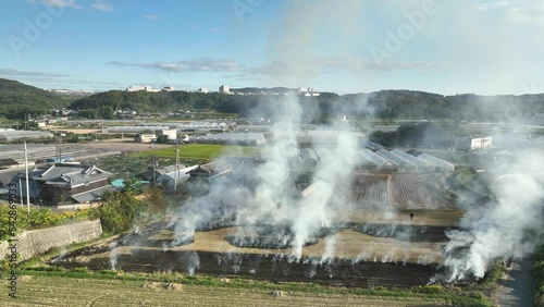 Smoke rises from smoldering field next to farm houses in countryside