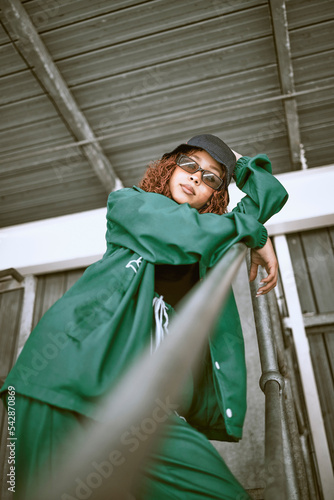 Obraz na plátně Fashion, street style and woman with green clothes, sunglasses and hat standing on stairs of an urban city building