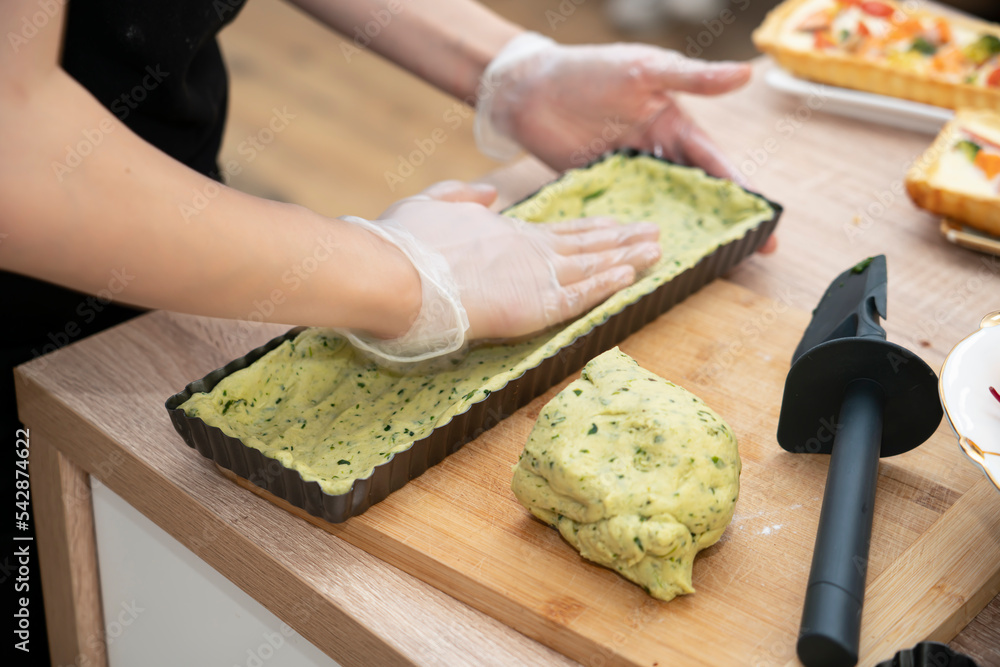 Cooking quiche with salmon. A woman puts spinach dough into a pie pan.