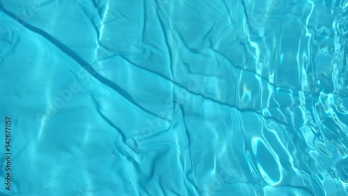 Clear blue water in an inflatable swimming pool glistens in the sun. Close-up top view background