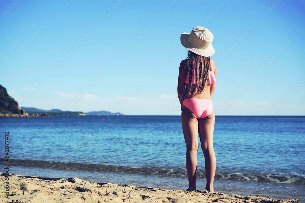 Girl in a hat and swimsuit on the seashore on the beach looks at the horizon Girl in a hat and swimsuit on the seashore on the beach looks at the horizon
