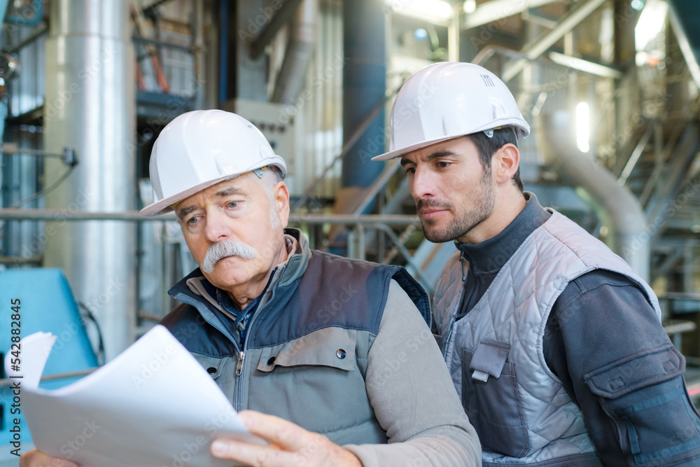 two male workers consulting paperwork on industrial site two male workers consulting paperwork on industrial site