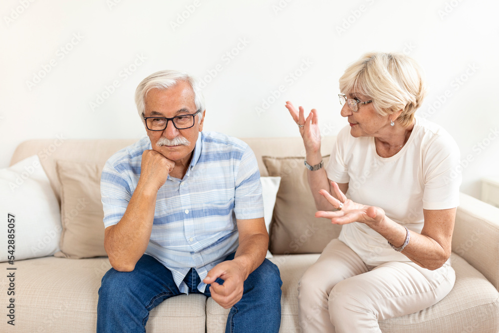 Senior couple having argument on the couch at home in the living room. Woman and man emotions gesturing with hands. Senior couple arguing