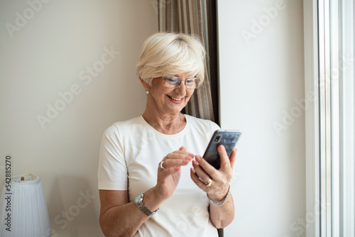 Beautiful senior woman at home talking on cell phone. Cheerful woman making a phone call and looking out the window Technology, communication and people concept