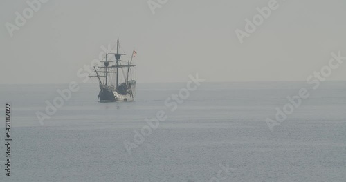 Ferdinand Magellan Nao Victoria carrack boat replica with spanish flag sails in the mediterranean at sunrise in calm sea exiting the frame in slow motion 60fps photo
