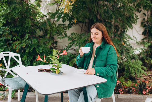 Portrait of beautiful woman drinking a cup of tea in cafeteria. Young caucasian Redhead woman in a cafe drinking coffee, happy emotions.
