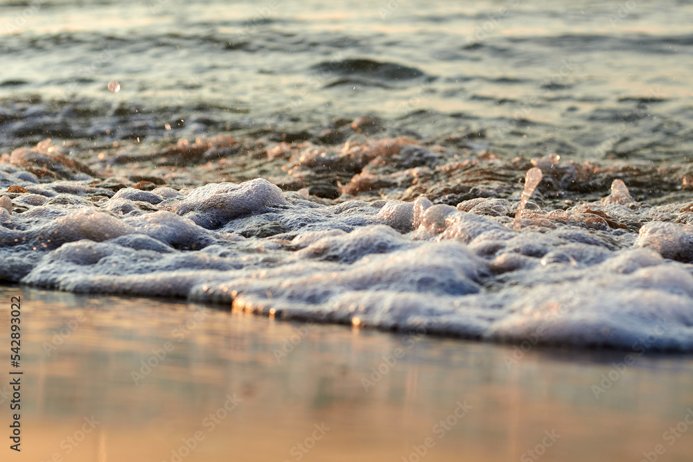 Close-up foam of sea waves on a yellow sandy beach. Beach morning wave wash up sand shoreline sea water sunlight reflections Close-up foam of sea waves on a yellow sandy beach. Beach morning wave wash up sand shoreline sea water sunlight reflections