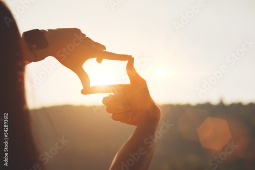 Planning and vision concept of new year's start, woman hands making frame gesture find focus at sunset, woman looking for perspective to capture the meaning of a clear upcoming target.