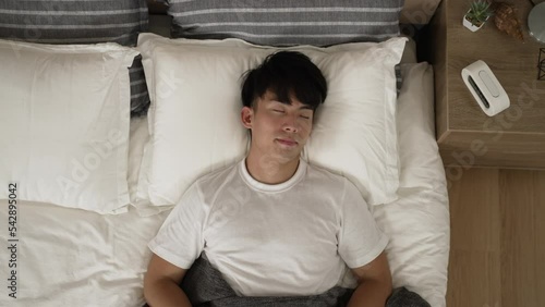 top angle view of a Korean man sleeping peacefully on the white comfortable mattress in bed at a modern home bedroom interior.