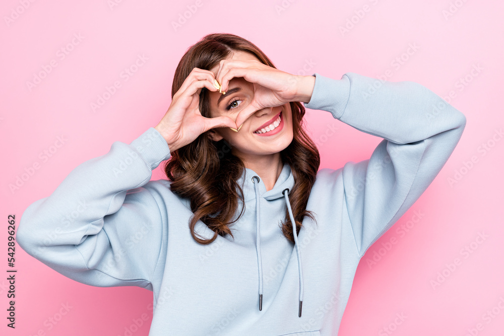 Photo of positive funny young lady wear grey hoodie looking showing arms heart isolated pink color background Photo of positive funny young lady wear grey hoodie looking showing arms heart isolated pink color background
