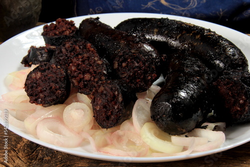 Baked black pudding with pickled onions on a white plate. Sliced and fried blood sausage on a plate photo