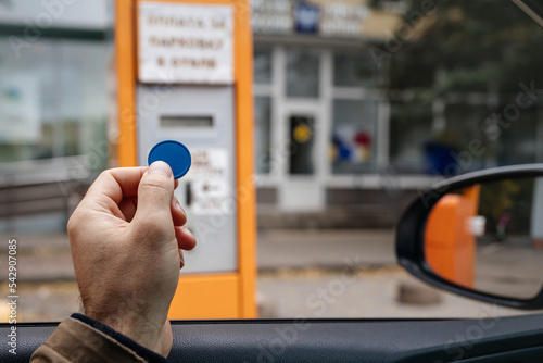 A token for paying for a car parking space in a man's hand from the window. On-site parking toll machine.