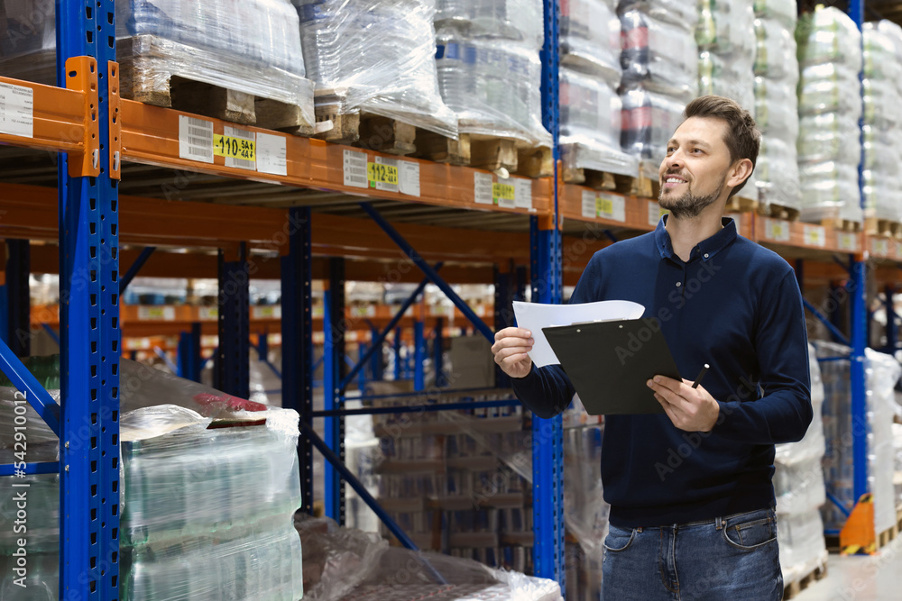 Happy manager holding clipboard in warehouse with lots of products