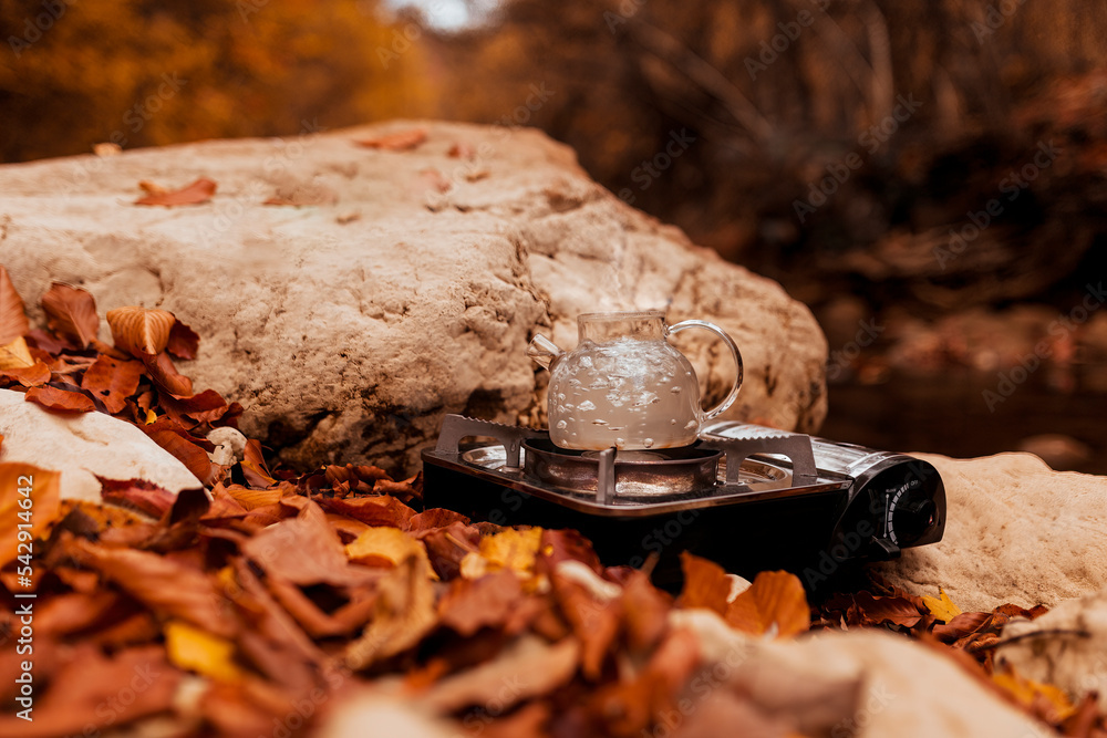 water boils in a teapot on a portable gas stove on a stone in the autumn forest