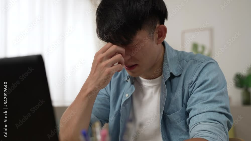 slow motion of a stressed asian male suffering a blurred vision is massaging his eyes and having trouble seeing clearly while working from home on the computer. slow motion of a stressed asian male suffering a blurred vision is massaging his eyes and having trouble seeing clearly while working from home on the computer.