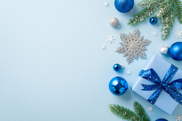 New Year concept. Top view photo of blue silver baubles big present box with ribbon bow glitter snowflake ornament fir branches in snow and confetti on isolated pastel blue background with copyspace