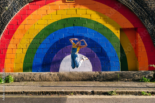 Cheerful transgender person jumping in front of rainbow wall photo