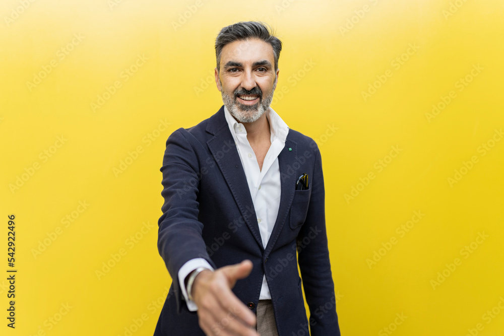 Smiling businessman doing handshake against yellow wall Smiling businessman doing handshake against yellow wall
