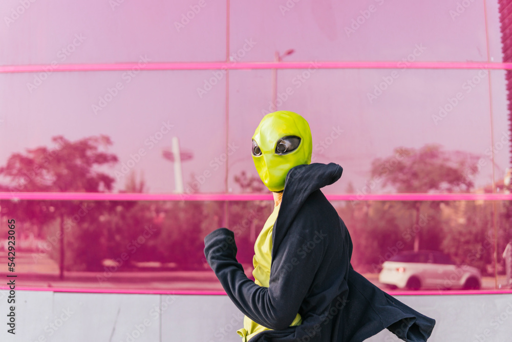 Man wearing alien mask running in front of pink glass wall foto de