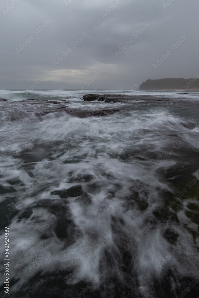 Cloudy view of the rocky coastline with high tide water flowing.