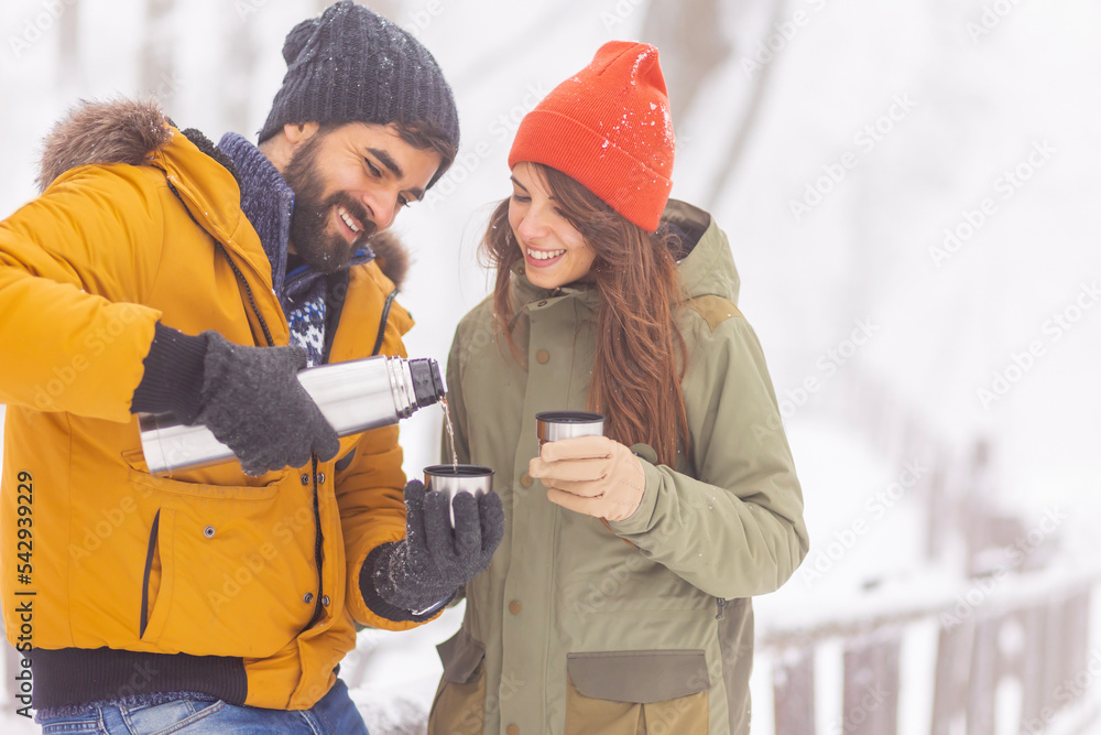 Couple spending snowy day outdoors drinking hot tea Couple spending snowy day outdoors drinking hot tea