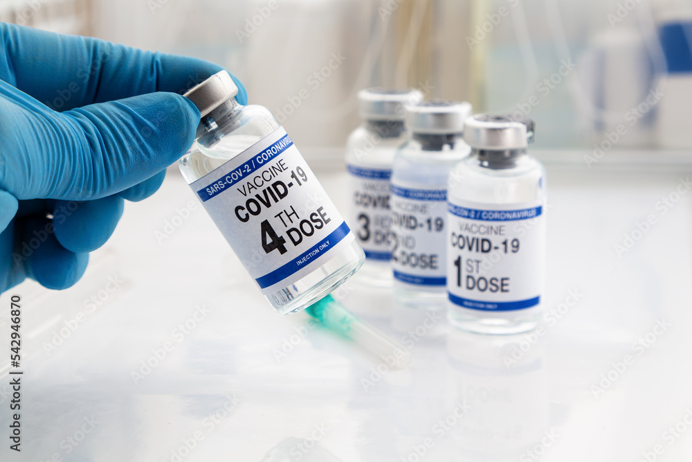 Hand holding COVID-19 Vaccine Vial for vaccination tagged with 4th dose and background 1st, 2nd, 3rd, vaccines. Doctor holding Coronavirus vaccine bottle with name of fourth dose of vaccine on label Hand holding COVID-19 Vaccine Vial for vaccination tagged with 4th dose and background 1st, 2nd, 3rd, vaccines. Doctor holding Coronavirus vaccine bottle with name of fourth dose of vaccine on label