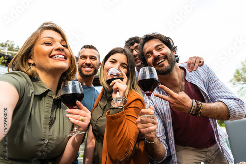 Happy group of Friends taking selfie while toasting red wine - Group of happy friends taking selfie using mobile smart phone camera - Young people having fun a drinking red wine outdoor photo