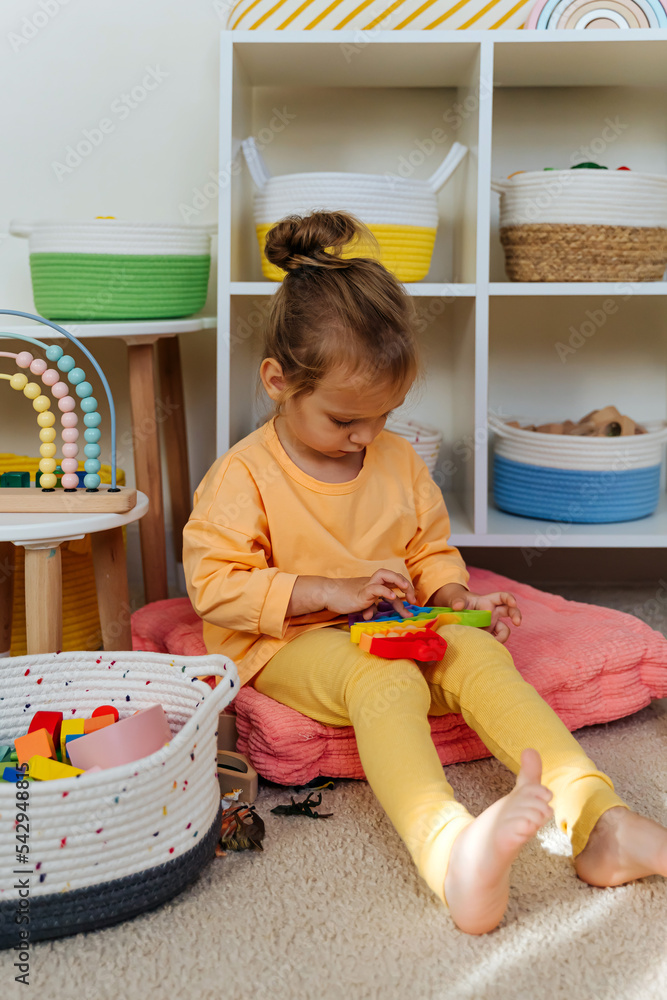 Sitting Fidget Child sitting on floor playing with the Pop It in childrens room. Push ...