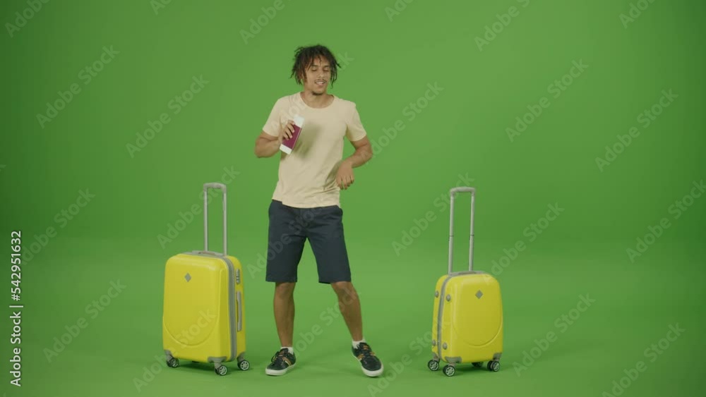Funny Young Mexican Traveller Ritmically Dancing from Foot to Foot between 2 Yellow Trolley Bags with Tickets and Passport on Green Screen Background.Tourist is Happy to Come in Time before the Flight Funny Young Mexican Traveller Ritmically Dancing from Foot to Foot between 2 Yellow Trolley Bags with Tickets and Passport on Green Screen Background.Tourist is Happy to Come in Time before the Flight