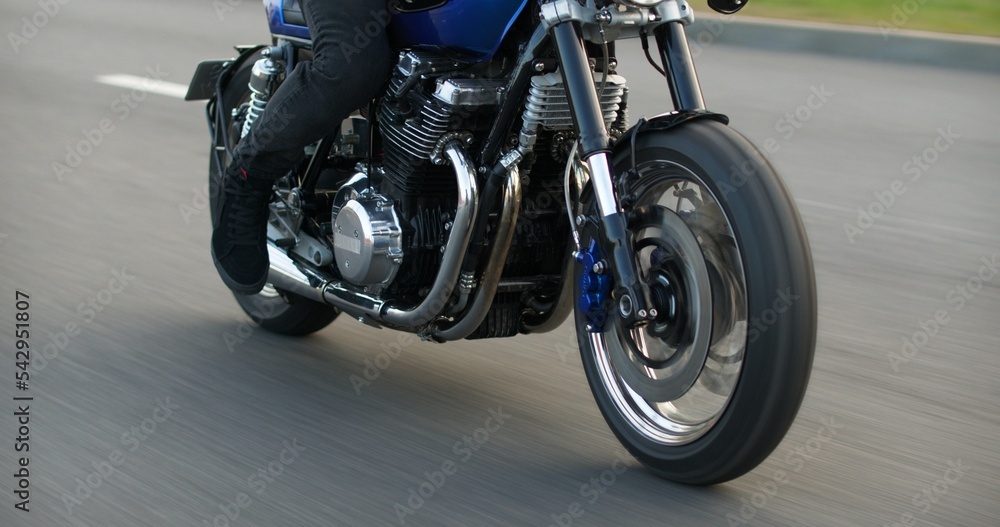 Close-up of a motorcycle riding on a road at high speed. Side view. Driving Bike on Streets. Speed Motion in Cityscape. Fast TRACKING Shot of a biker riding his custom built cafe racer through city.