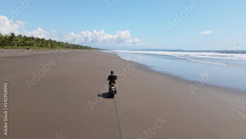 Young man on scooter riding over the hard sand of a wide, long tropical beach. Wide angle tracking shot photo