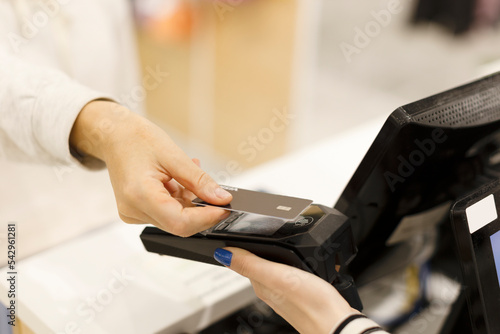 Hands hold a credit card and pay for purchases in the store. Credit card in hand, hands, point of sale, purchases in the store. A woman buys goods in a supermarket.