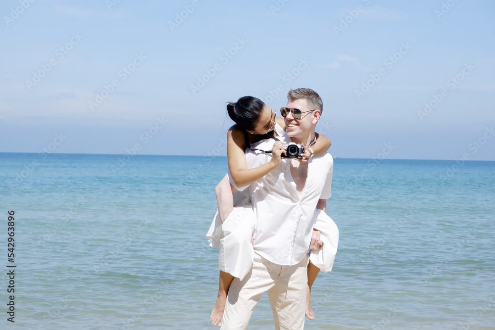 Happy smiling young couple walking on the beach holding a camera love concept travel.