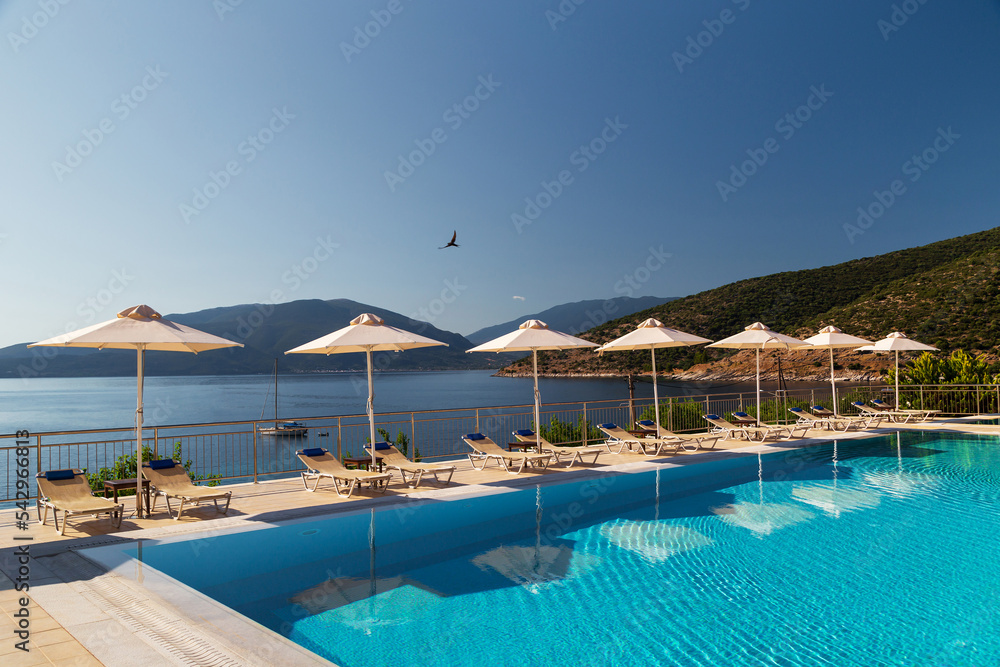Luxury swimming pool with empty deck chairs and umbrellas at resort with beautiful sea view. Greek islands.