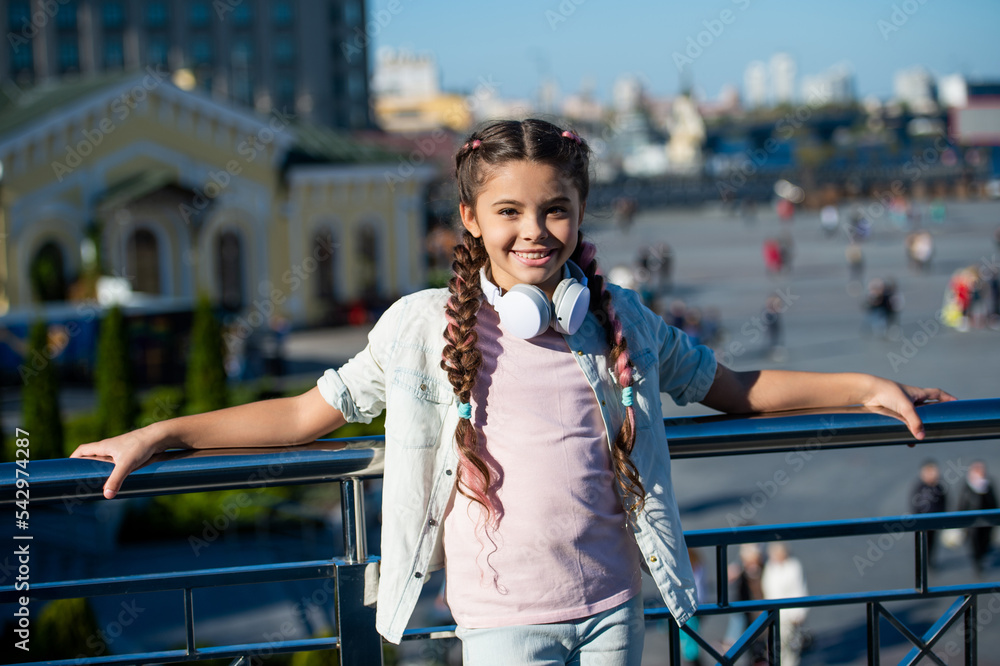 Happy girl leaning against railing. Teenage girl with pigtails smiling outdoors. Adolescent girl