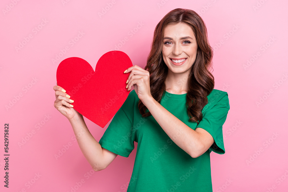 Portrait of adorable girlish nice girl with curly hairstyle wear green t-shirt hold big paper red heart isolated on pink color background Portrait of adorable girlish nice girl with curly hairstyle wear green t-shirt hold big paper red heart isolated on pink color background