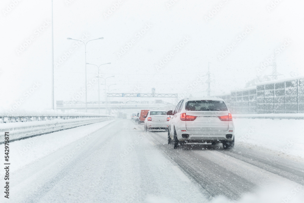 Scenic view snow covered intercity highway slippery snow covered road drive cars moving slowly. Snowfall danger blizzard bad winter weather conditions. Urban cold snowy day snowstrom town background Scenic view snow covered intercity highway slippery snow covered road drive cars moving slowly. Snowfall danger blizzard bad winter weather conditions. Urban cold snowy day snowstrom town background