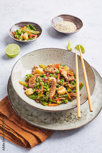 Wok with turkey meat, corn, green peas, green beans and carrots served on gray background with chopsticks. Asian food concept of street food