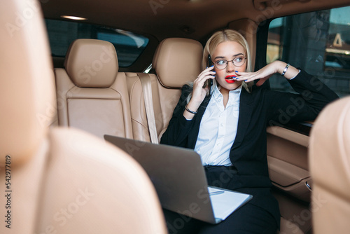 A beautiful businesswoman is talking on the phone and working at a computer in the car